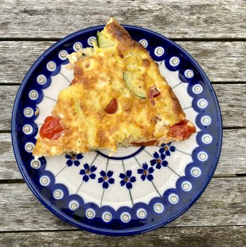 A slice of Italian veggies frittata on a blue and white plate, with a table background